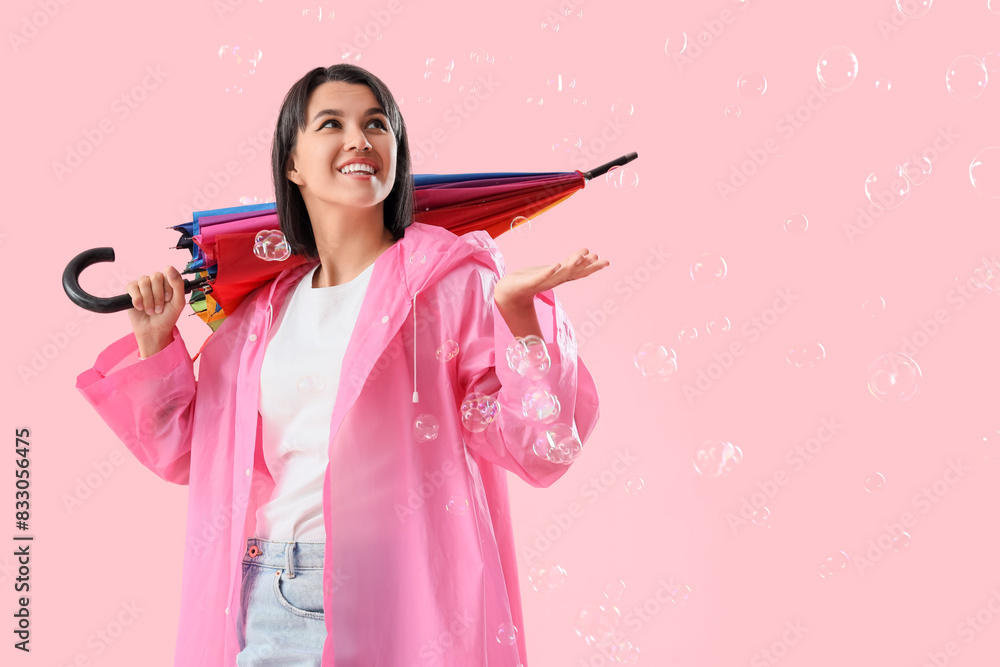 Happy young woman in raincoat with umbrella and soap bubbles on pink background Happy young woman in raincoat with umbrella and soap bubbles on pink background