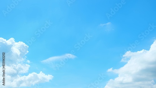 A bright blue sky with a few fluffy white clouds. The clouds are primarily gathered at the edges  leaving the center of the sky clear and vibrant  creating a calm and peaceful atmosphere. 