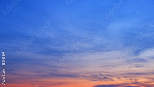 A stunning sunset with a sky that transitions from deep blue at the top to warm orange and pink hues near the horizon. The clouds add texture and depth to the tranquil scene. Sunrise sky background. 