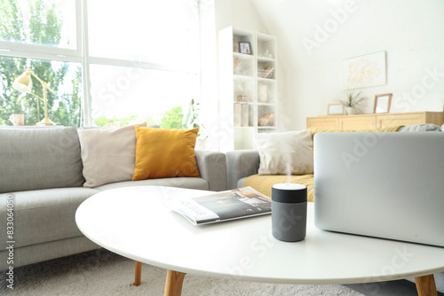 Air humidifier with laptop and magazine on table in living room  closeup