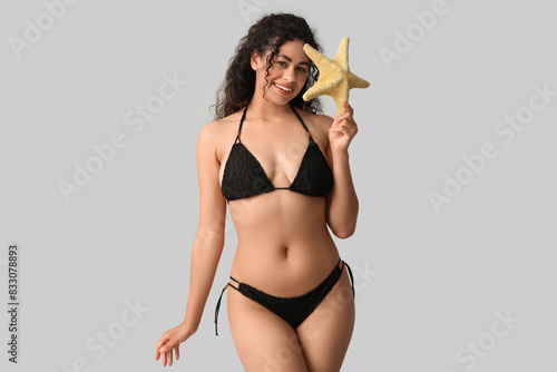 Beautiful young African-American woman in stylish black swimsuit with starfish on grey background