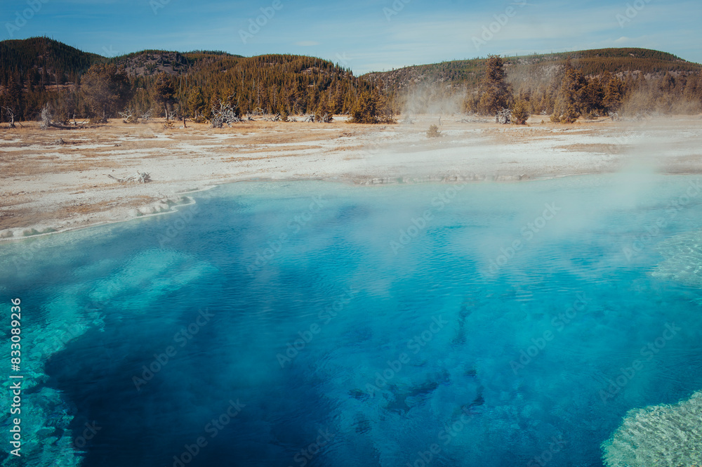 Sapphire blue geothermal pool amidst steaming hot springs on a bright day.