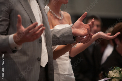 A closeup moment of a bride and groom joining hands to pray at a wedding ceremony in a church backdrop