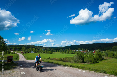 Cycling trip in Sweden, Cyclist on touring bicycle solo travel Nordic countryside, Road among fields summer day, Long distance cycling travel around the world, Mangskogsvägen south of Tobyn, Värmland