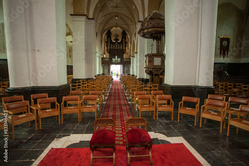 Symmetrical view of a historic church interior featuring wooden chairs, red carpet, and ornate architecture.
