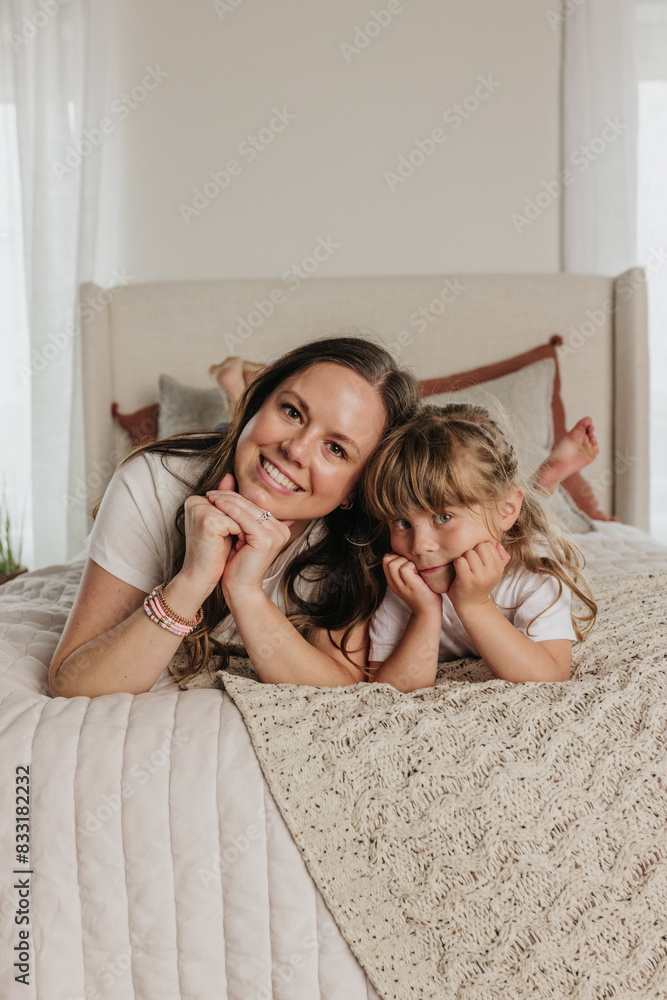 Mom and daughter lay on bed together while resting heads on hands Mom and daughter lay on bed together while resting heads on hands