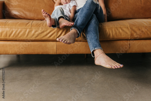 Faceless photo focus on feet of mother and daughter snuggled on couch photo