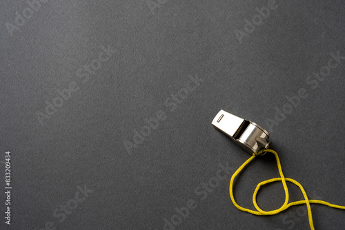 Top view of metal whistle with yellow string on dark gray background photo