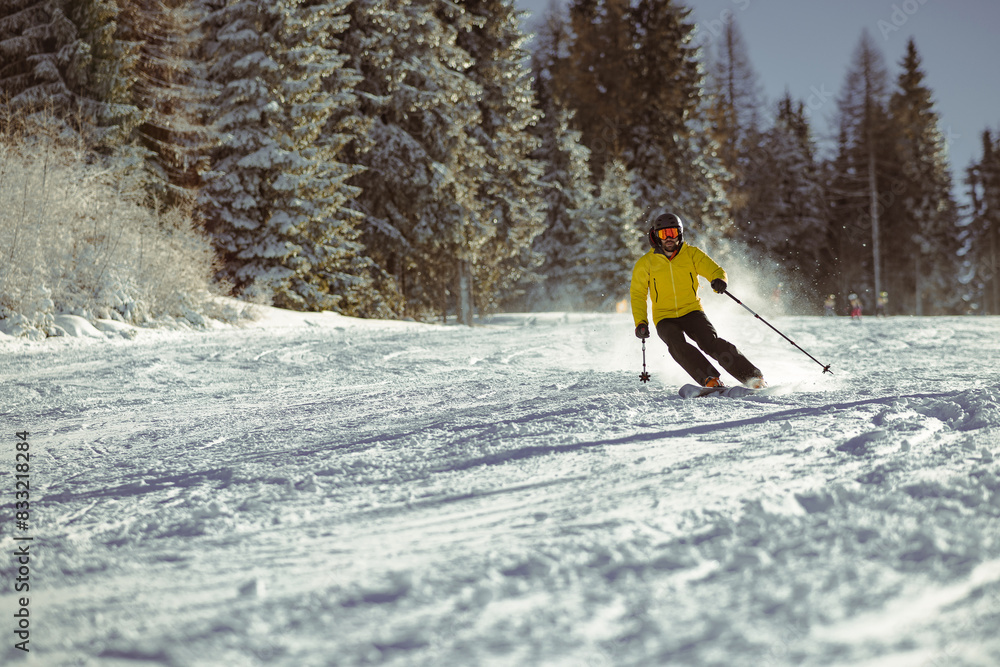 Young person in fashionable clothes is skiing towards the camera on a ski slope on a sunny day. Carve or carving on ski piste, perfect weather, strong backlight.