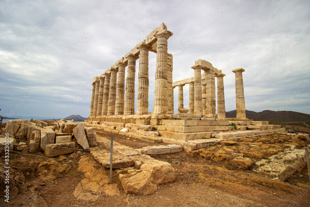 Fototapeta premium Majestic Ruins of the Ancient Temple of Poseidon at Cape Sounion Under Cloudy Skies Overlooking the Aegean Sea