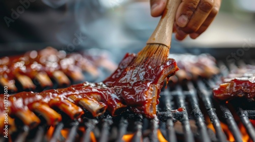 Close-up of a chef's hand basting pork spare ribs with BBQ sauce on a grill, with sizzling sounds photo