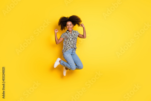 Photo of glamour young woman curly hair in zebra print shirt jump air raised fists up winning tournament isolated on yellow color background photo