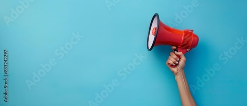 A human hand holding a vibrant megaphone against a solid blue backdrop with ample copy space