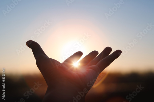 Hands stretched out toward the rising sun at New Year's sunrise, brilliant light shining between fingers, future hope and hope concept
