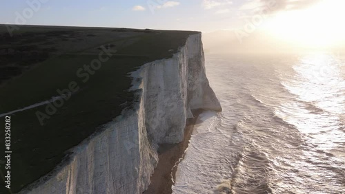 Majestic white cliffs overlook the ocean, with golden light of sunset. Waves crash dramatically below, creating a serene and picturesque landscape that captivates nature enthusiasts. Seven Sisters 