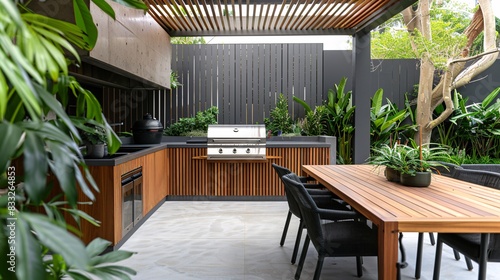 Fototapeta Naklejka Na Ścianę i Meble -  A modern outdoor kitchen with wood accents, featuring an island table and grilling station, surrounded by plants in the backyard of an Australian home. The space is designed for social gatherings