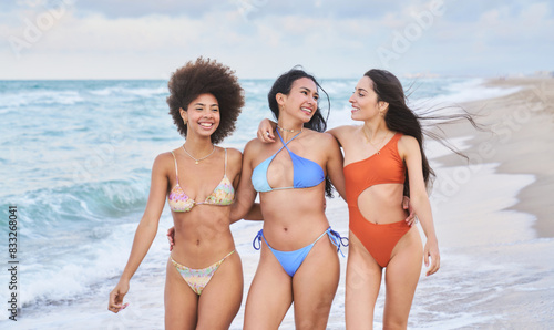 Three women are walking on the beach in bikinis