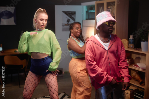 Portrait of dance performers wearing colorful outfits recording content videos for social media indoors with dim lighting