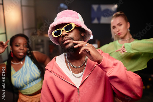 Waist up portrait of contemporary dance crew indoors with focus on Black man wearing pink outfit looking at camera with style
