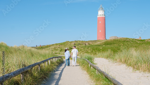 A couple leisurely walks along a winding path near the iconic Texel Lighthouse  enjoying the scenic coastal views on a peaceful day. man and woman at The iconic red lighthouse of Texel Netherlands
