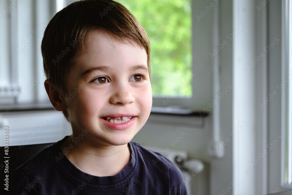 Happy 6 year old boy child is smiling enjoying life. Concept of happy childhood. Portrait of young sitting boy in home background, indoors. Adorable face. Nice smile with beautiful teeth. Side view Happy 6 year old boy child is smiling enjoying life. Concept of happy childhood. Portrait of young sitting boy in home background, indoors. Adorable face. Nice smile with beautiful teeth. Side view