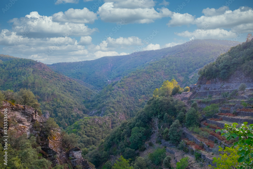 A stunning view of a mountain valley showing terraces, lush greenery, and a vibrant sky with clouds