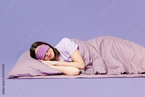 Fotografía Side profile view young calm woman wears pyjamas jam cover eyes with sleep eye mask rest relax at home lay down on bed isolated on plain pastel purple background studio