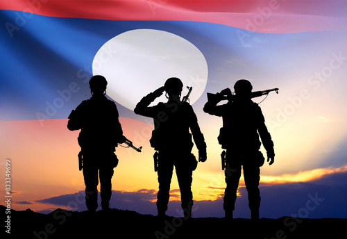 Silhouettes of a soldiers with Laos flag against the sunset. Armed Force of Laos. National Holidays concept © ecrow