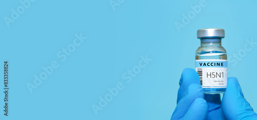 A doctor in blue gloves holding a bottle with vaccine vial of H5N1.Bird flu vaccine. The concept of medicine, healthcare and science. Banner. Copy space for text