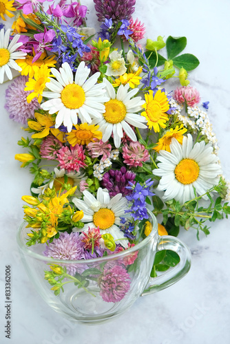 colorful flowers and herbs in glass cup on table close up. floral tea, organic healthy beverage. Flavor useful herbal tea from natural wild plants. alternative medicine concept. top view