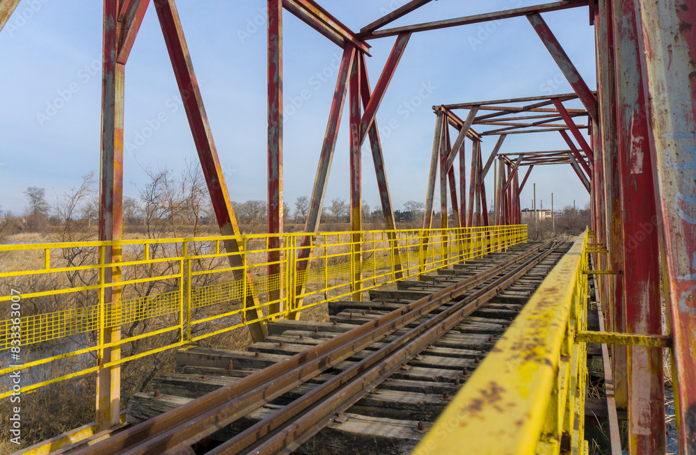 Yellow railings, high beams, old rusty rails, brown wooden sleepers of a railway bridge. Blue sky Yellow railings, high beams, old rusty rails, brown wooden sleepers of a railway bridge. Blue sky
