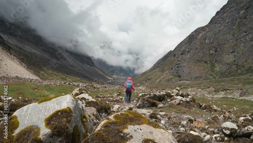 Lonely woman backpacker trekker dressed bright jacket going by mountain valley path on the Mera peak climbing route near Tagnag settlement at cca 4150m. Active people wide mountain valley 4K video. photo