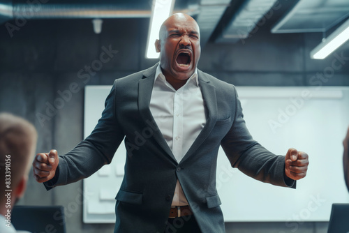 Angry man in suit yelling with clenched fists in office. He is standing and appears to be shouting at people in front of him