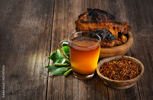 Chaga mushroom pieces and chaga mushroom tea with birch leaves on a wooden background.