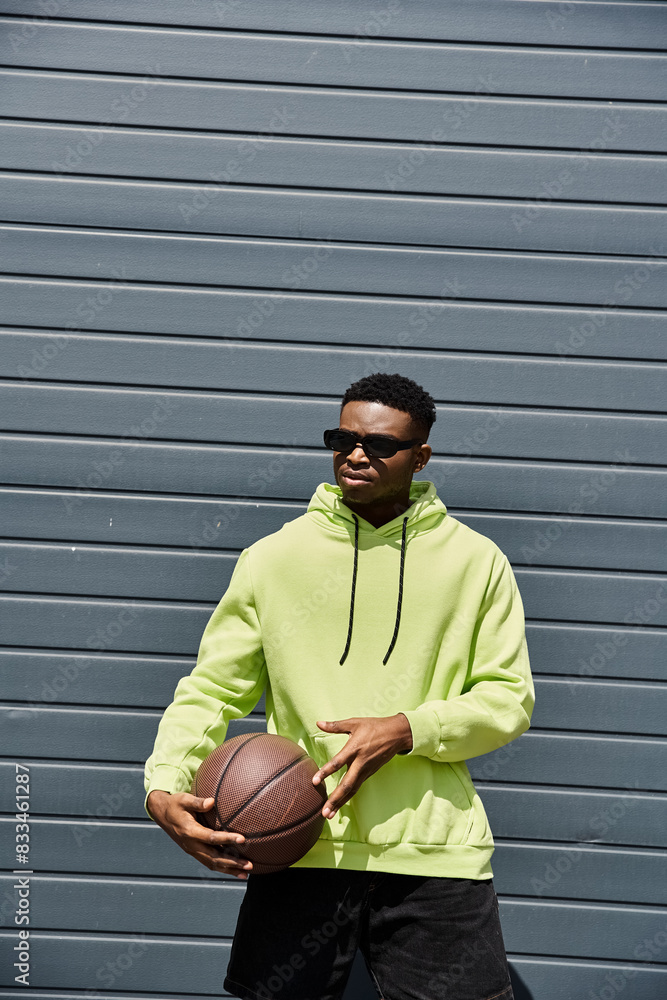 Young African American man in neon green hoodie holds basketball.