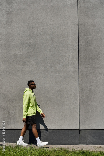 A fashionable young African American man walking in front of a gray wall.
