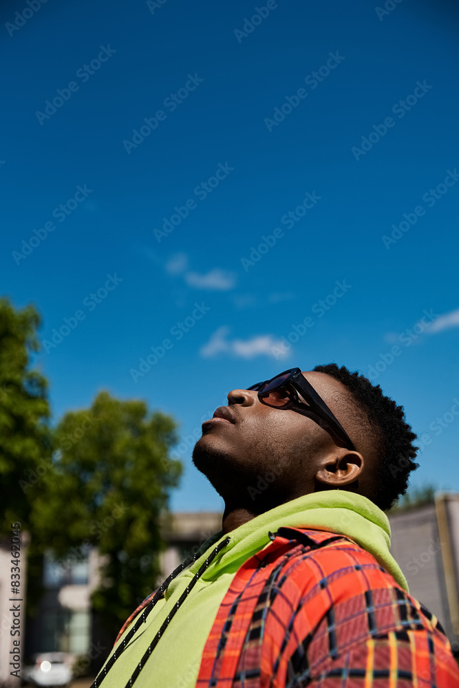 Young African American man in plaid hoodie and sunglasses gazes at the sky. Young African American man in plaid hoodie and sunglasses gazes at the sky.