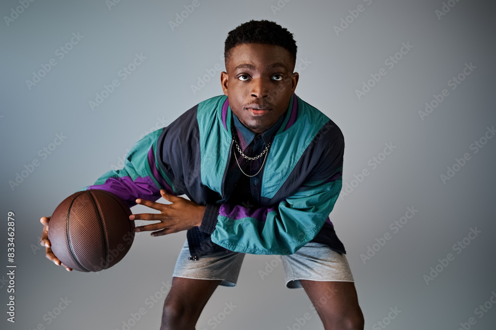 Stylish young African American man holding a basketball against a gray background. Stylish young African American man holding a basketball against a gray background.