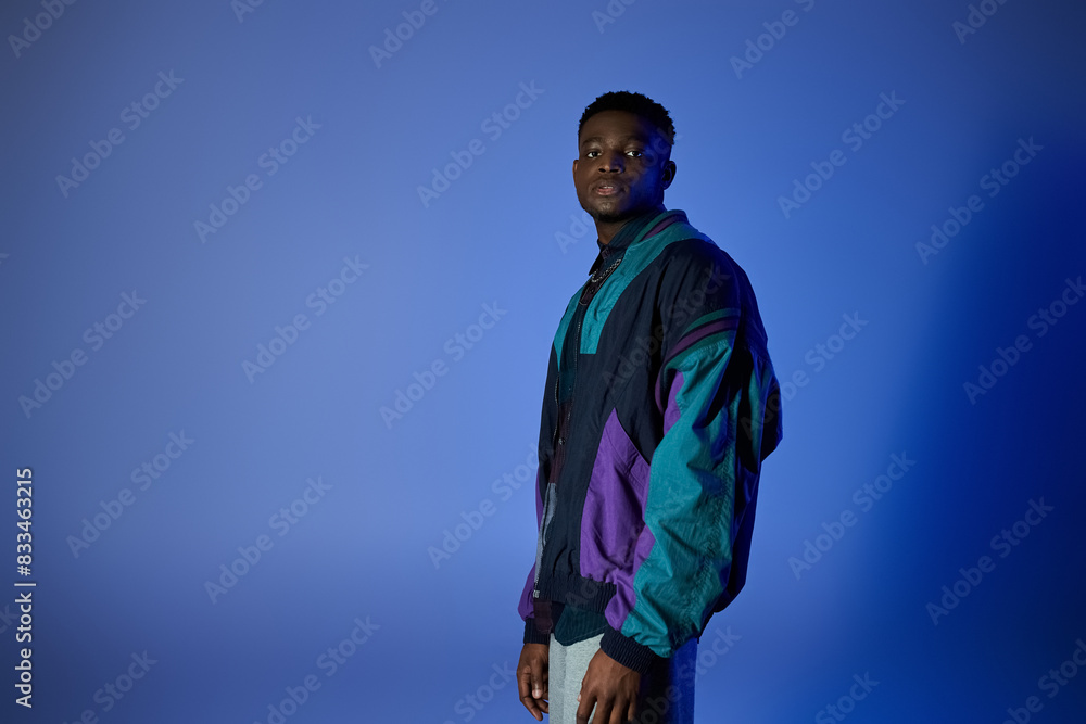 African American man wearing colorful jacket, standing against blue backdrop. African American man wearing colorful jacket, standing against blue backdrop.