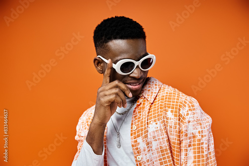 Handsome African American man in sunglasses poses stylishly on orange background.
