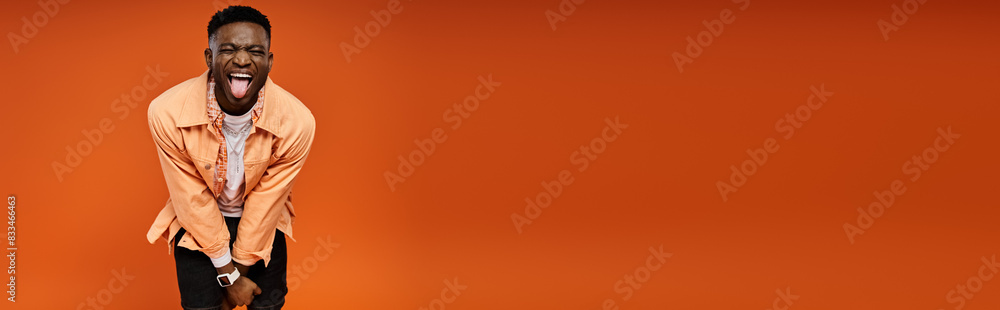 Obraz premium Fashionable African American man poses gracefully against bold orange background.