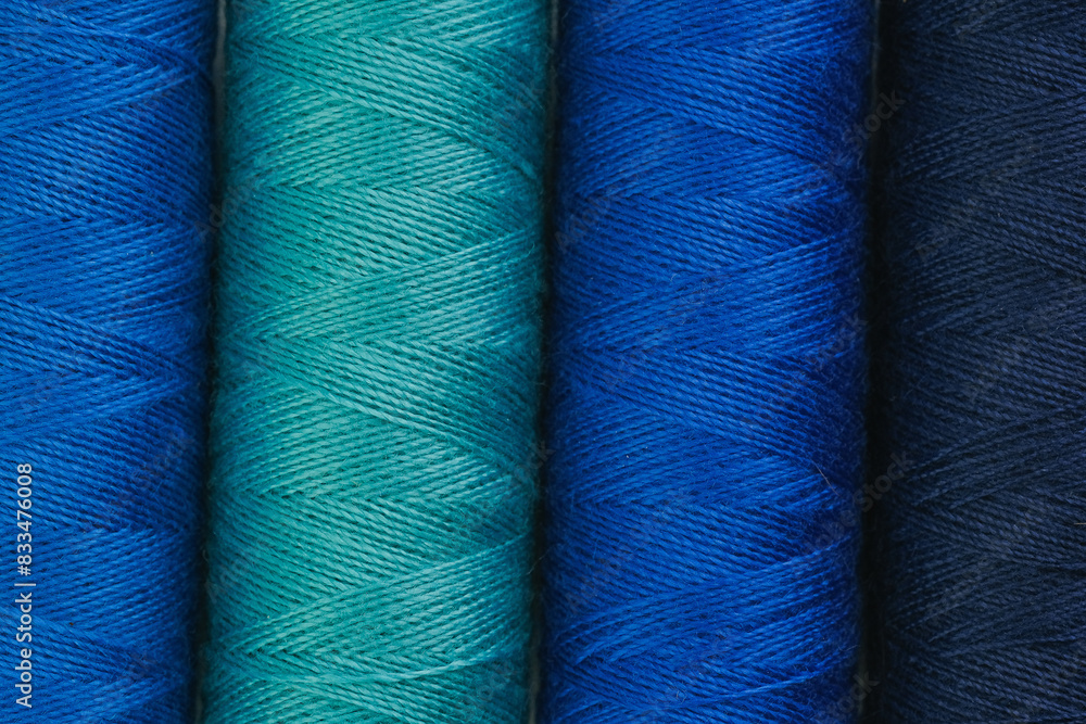 Various spools of blue and green yarn neatly arranged in a row Various spools of blue and green yarn neatly arranged in a row