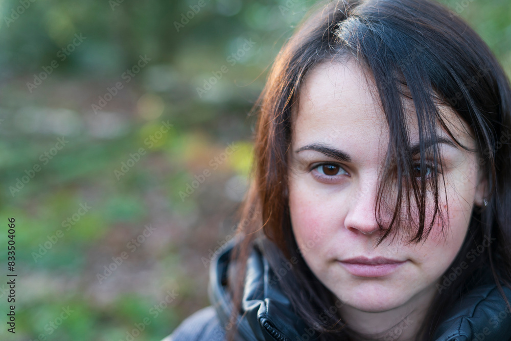 Close-up portrait of a beautiful dark-haired girl in a black jacket and backpack standing in the forest Close-up portrait of a beautiful dark-haired girl in a black jacket and backpack standing in the forest