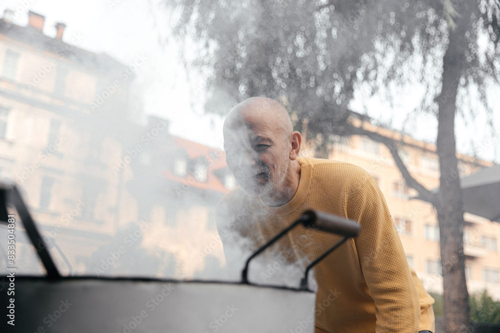 Senior Man in Yellow Sweater Engaged in Outdoor Cooking on an Urban Street.. Senior Man in Yellow Sweater Engaged in Outdoor Cooking on an Urban Street..