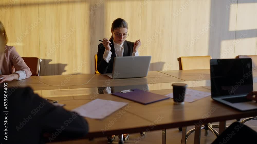 A tired girl in round glasses and a business uniform a businesswoman, sits at the table and tries to relax during a hard day at work with her colleagues A tired girl in round glasses and a business uniform a businesswoman, sits at the table and tries to relax during a hard day at work with her colleagues