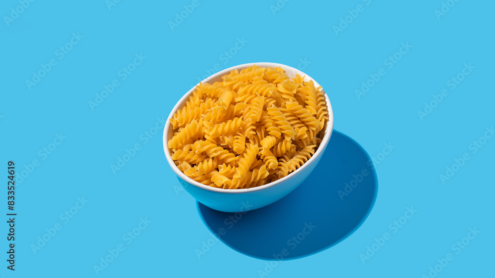Uncooked fusilli pasta spirals in a white bowl on a blue background Uncooked fusilli pasta spirals in a white bowl on a blue background