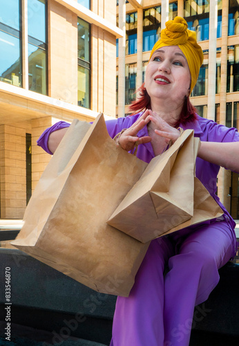 Obraz na płótnie woman with craft shopping bags in the city. The concept of fashionable Consumerism and ecology. An adult Asian woman in a purple suit with red and yellow accents enjoys shopping . a sunny day. w salonie