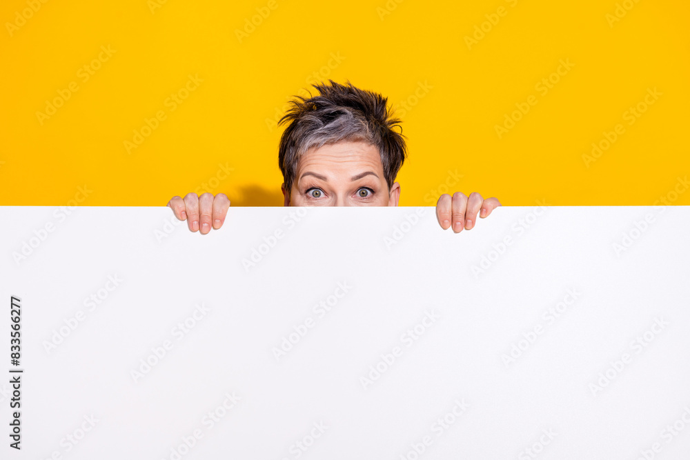 Portrait of nice aged lady hide behind empty space wear t-shirt isolated on yellow color background Portrait of nice aged lady hide behind empty space wear t-shirt isolated on yellow color background