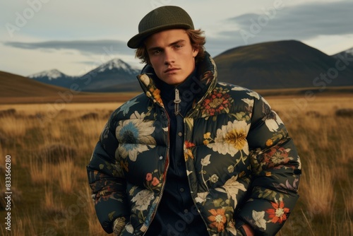 Fashionable young man poses in a floral jacket against a serene mountainous landscape at dusk