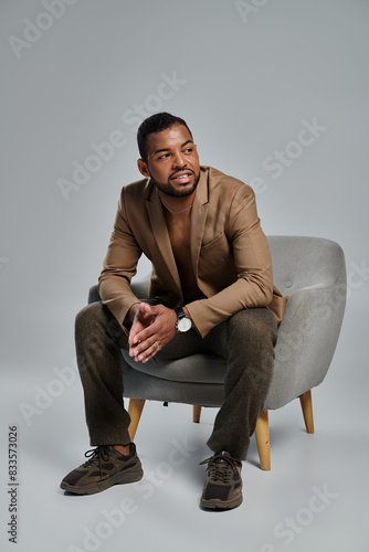 A man gracefully sits atop a gray chair in a contemplative pose. photo